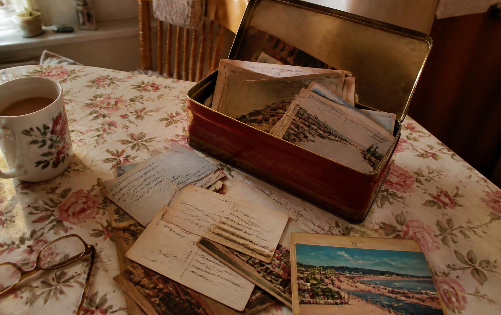 An old tin box tipped open on aged parchment, spilling out vintage handwritten postcards, stamps and postmarks